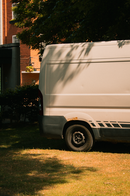 A collection of three cardboard moving boxes with printed handling and fragility symbols, resting on a paved surface in front of a grey garage door. Two of the boxes are positioned on a hand truck wit